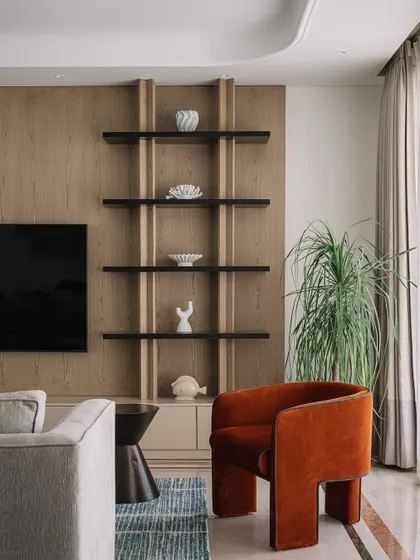 This living room showcases our ability to create bold focal points. The rust-colored armchair was custom-made to add a pop of color and sculptural form, while the sleek shelving unit provides a minimalist backdrop, demonstrating how we balance different design elements.