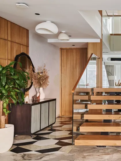 The entrance foyer features geometric black, white, and beige floor tiles and a custom console table. A floating wooden staircase with glass railings leads to the upper floor.
