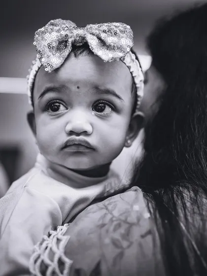 A poignant black and white close-up of a baby girl with a sequined bow, her expressive eyes telling a story. We use monochrome to highlight emotion.