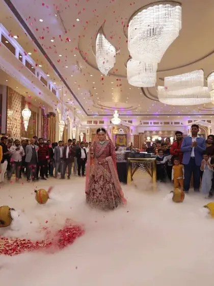 A bride's grand entrance, walking on a cloud of low fog surrounded by her loved ones in a beautifully lit banquet hall.