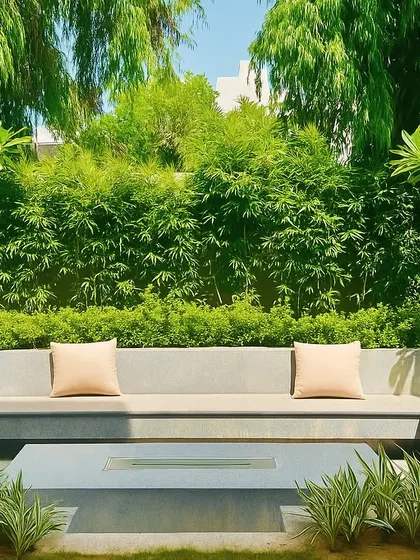 A minimalist concrete fire pit and built-in seating area, surrounded by a dense wall of bamboo and other greenery. This creates a modern yet natural space for relaxation.