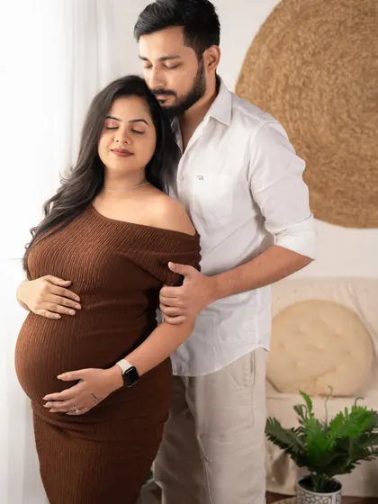 A moment of quiet reflection. The father-to-be gently holds his partner, both looking down at the baby bump with love and tenderness.