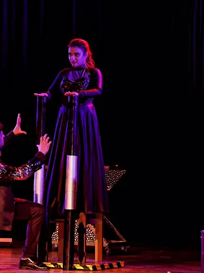 A photograph of the chair levitation illusion from a theatre show. The dramatic lighting and staging help create a powerful and unforgettable visual for the audience.