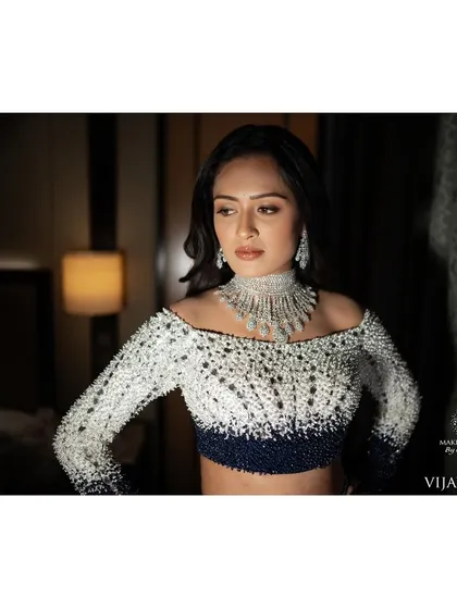 A close up of Ashitha's reception look. The makeup features a sharp, clean eye and flawless skin, complementing the intricate beadwork of her off shoulder blouse.