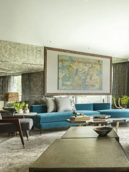A wide view of the Jor Bagh Residence living room, showcasing a balance between modern aesthetics and comfort. A large traditional painting is given a contemporary frame, and a brass-paneled wall adds a touch of glamour.