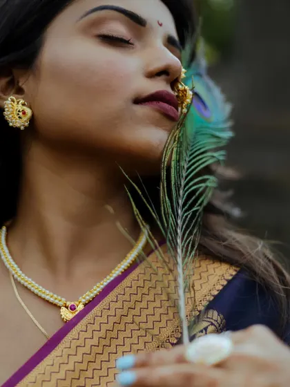 A creative close-up using a peacock feather as a prop. This artistic portrait highlights the model's traditional jewelry and the rich texture of her saree, creating a connection to cultural symbolism.