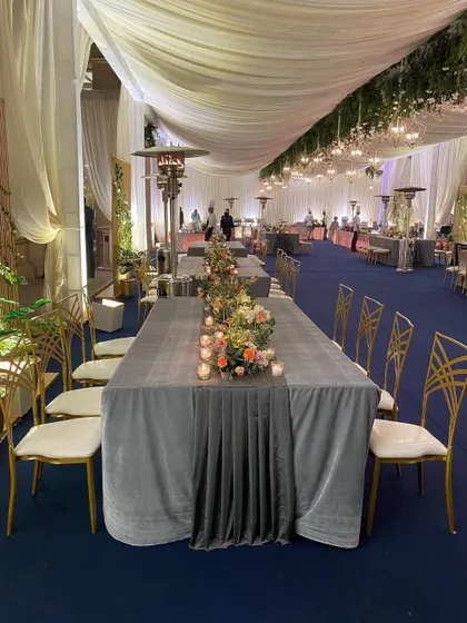 A close-up of the elegant dining setup for a reception. The long table is dressed in a grey velvet runner and simple candle arrangements, set against a deep blue floor for a look of understated luxury.