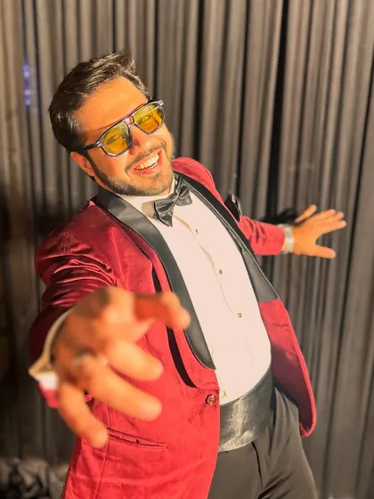 Reaching out to the audience with a big smile, dressed in a show-stopping red tuxedo.