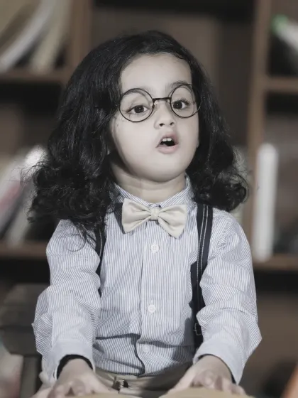 A thoughtful black and white portrait of a young boy with glasses, giving him a wise and studious look.