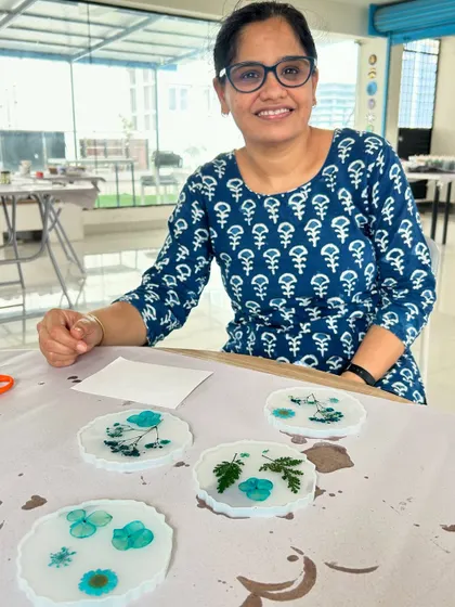 A participant proudly displays her set of four delicate pressed flower coasters made with white resin.