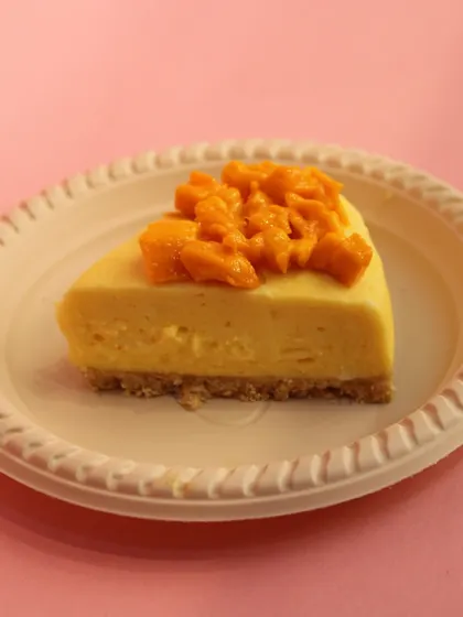 A simple, elegant slice of our seasonal Mango Cheesecake, topped with fresh, diced mangoes on a paper plate.
