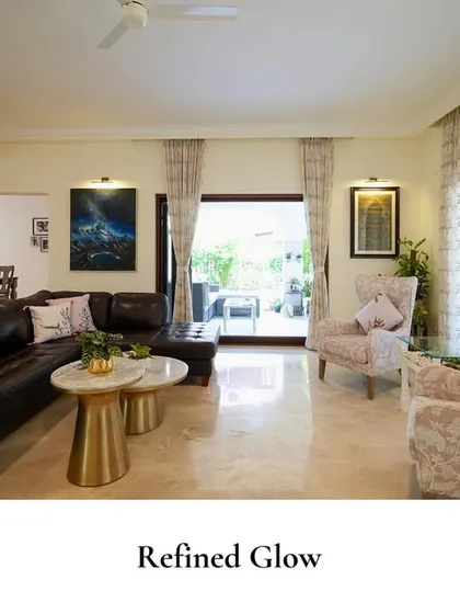This living room combines classic comfort with modern details, featuring a deep leather sectional, floral wingback chairs, and gold-accented tables on a polished marble floor.