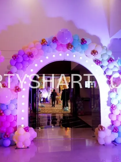 A beautiful lighted entrance arch for a butterfly party, decorated with a dense arrangement of pastel-colored balloons and a custom welcome sign.