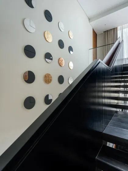 The staircase is more than a transition; it's a sculptural element. A collection of custom-made circular art pieces, finished with vegetable dyes and gold leaf, creates a dynamic installation along the wall, transforming the act of moving through the home into a visual experience.