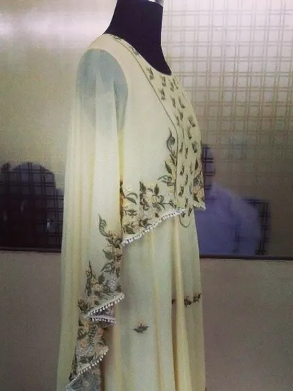 A side view of a beautiful off-white cape Anarkali. The design features delicate monochrome floral embroidery along the cape's scalloped edges, creating a flowing and ethereal silhouette.