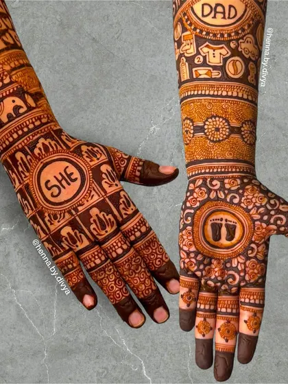 A fun gender reveal mehendi design. One arm features the word 'SHE' and the other 'DAD', with baby footprints and other cute symbols to celebrate the coming of a baby girl.