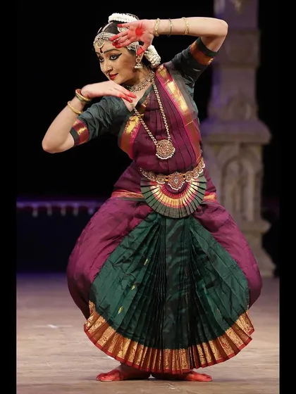 A full-body pose showing the combination of grace and strength that characterizes the depiction of Shiva in dance. The stage pillars add to the temple-like atmosphere.