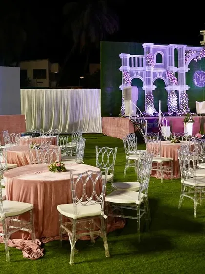 An overview of an outdoor reception setup, showing how we integrate large LED screens and grand stage designs. The blush pink table linens and clear Chiavari chairs add a touch of modern elegance to the space.