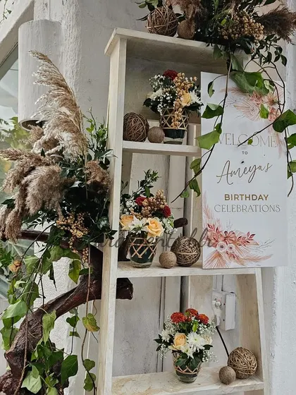A welcome setup for a boho-themed birthday celebration. A white ladder shelf is decorated with floral arrangements and a sign, creating a rustic and inviting entrance for guests.