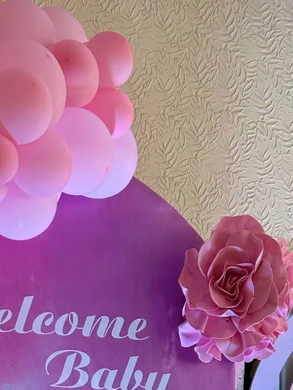 A close-up detail of a "Welcome Baby" sign, featuring a large paper rose and a pink balloon accent.