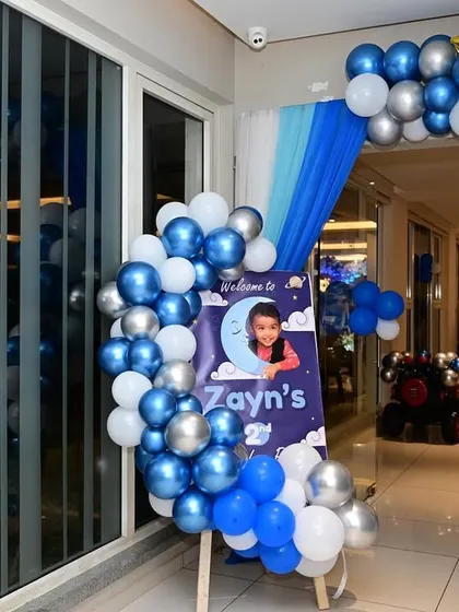 For this starry night theme, I created an entrance with a blue, white, and silver balloon arch. The personalized welcome board with the child's photo adds a lovely, personal touch.