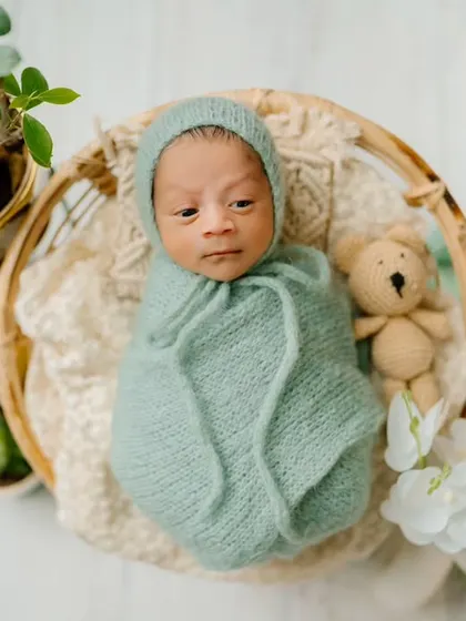 A tiny bundle of joy nestled in a basket. The soft green wrap and surrounding plants create a fresh, natural feel for this newborn's first photoshoot.