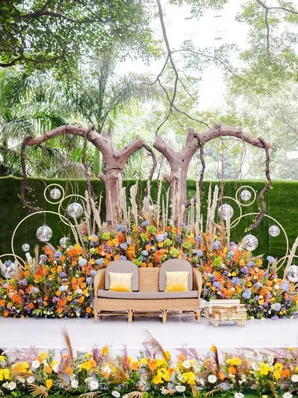 The full stage for the boho-chic Mehendi. The setup combines natural elements like wood and wicker with vibrant flowers and modern touches like disco balls, creating a unique and personalized space.