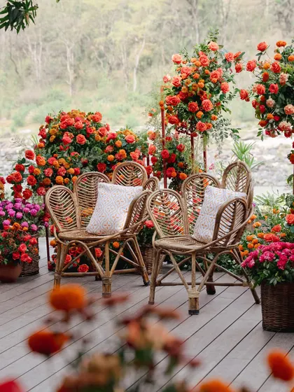 The couple's seating area, set on a wooden deck overlooking the river. The space is filled with marigolds and roses, with rustic cane chairs adding to the natural, earthy vibe.