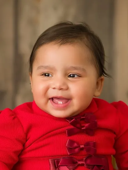 A close-up of the birthday girl's happy face. Her sweet smile and the festive red bows on her dress make this a perfect first birthday portrait.