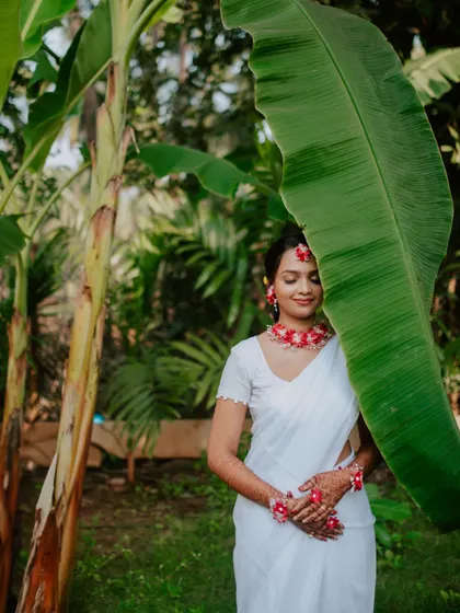 A creative bridal portrait during a Haldi ceremony, using a large banana leaf as a natural frame. This highlights the bride's serene glow against a lush, green backdrop.