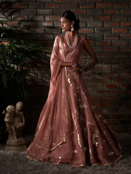 This dusty rose lehenga with gold foil work gently enhances the wearer's essence. The draped dupatta adds a touch of modern grace to the ensemble.