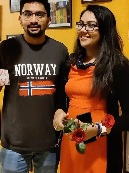 A happy couple celebrating their special day with us. They are holding a gift and roses, standing in front of our wall of classic movie posters.