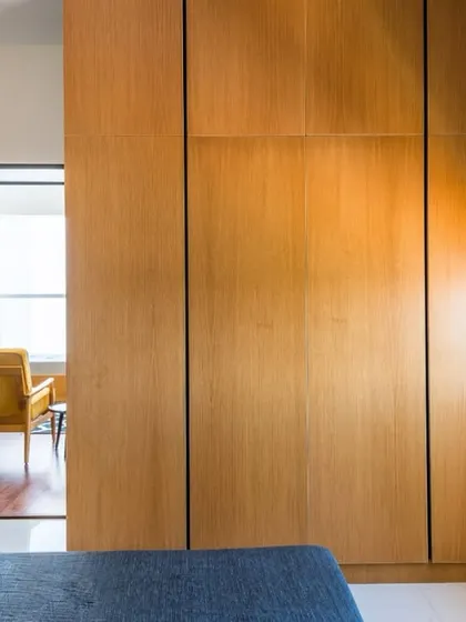 This cozy bedroom keeps things simple and elegant with natural wood-finish wardrobes and a pop of color from the blue bedding, with a view into the adjoining modern living area.