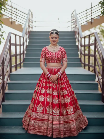 A stunning bridal portrait on a staircase, her red lehenga with lotus motifs spread out perfectly, creating a symmetrical and grand image.