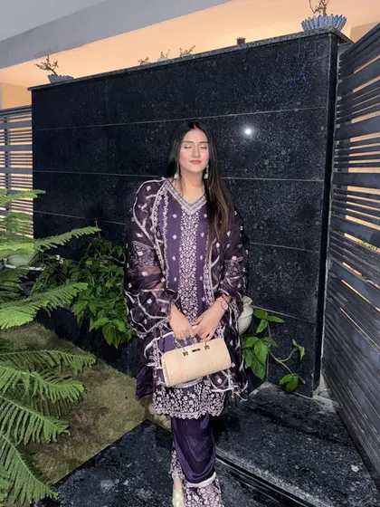Posing with a golden clutch that perfectly matches the festive vibe of the purple suit.