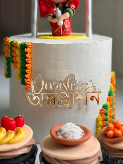 A close-up of the personalized nameplate on the Annaprashan cake, written in both English and Bengali.