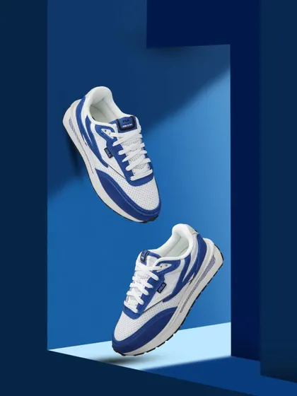 A pair of blue and white Fila sneakers appearing to float against a multi layered blue background, creating a sense of depth.