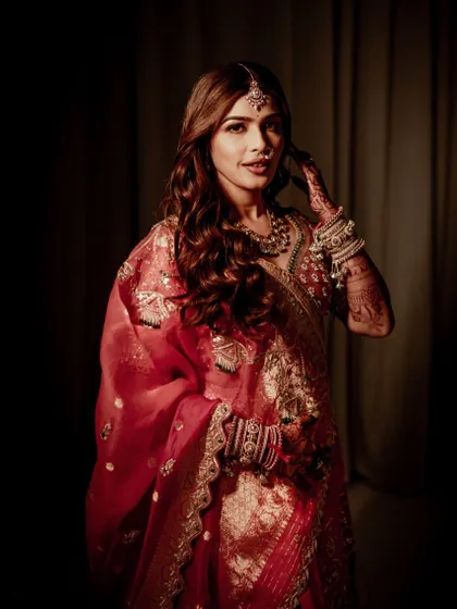 A dramatic portrait with deep shadows, making the bride's illuminated face and red attire stand out. The makeup is crafted to look stunning in any lighting condition.
