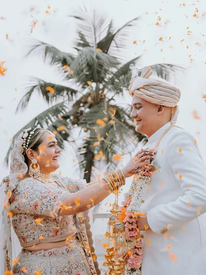 The Varmala ceremony against a beautiful outdoor backdrop. A shower of marigold petals rains down as the bride places the garland on the groom, creating a vibrant and joyful photograph.