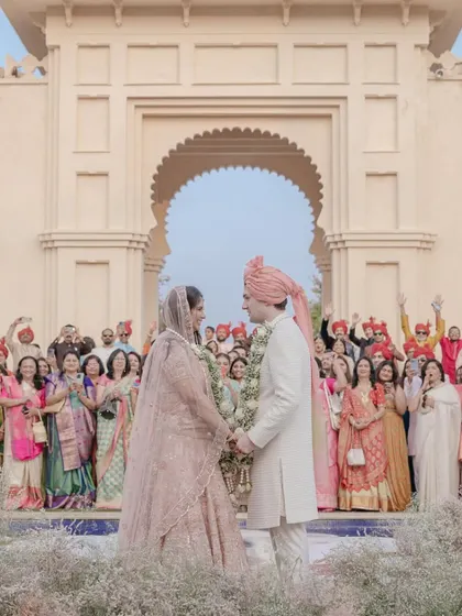 Pearl and James share a look after their varmala at the Oberoi Udaivilas in Udaipur. The stunning architecture and the cheering crowd create a perfect destination wedding moment.