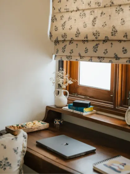 Our custom Roman blinds are a stylish alternative to curtains. This one, in a delicate floral print, adds a touch of elegance to a cozy home office nook, perfectly complementing the wooden desk and accessories.