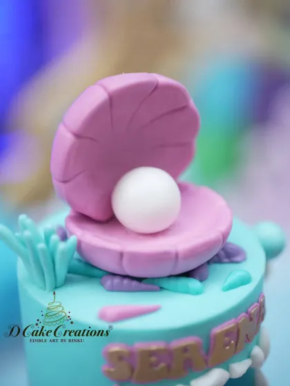 A macro shot of the delicate, handcrafted seashell and pearl topper, showcasing the fine details of our sugar art.