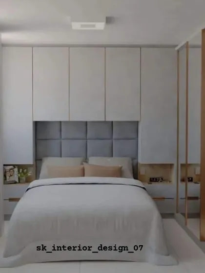 A cozy bedroom with a grey tufted headboard and integrated side niches. The mirrored wardrobe doors help to make the room feel larger and brighter.