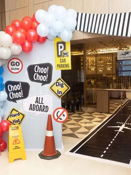 The entrance to the travel-themed party, designed with a runway floor decal, traffic signs, and balloon arches to welcome the little travelers.