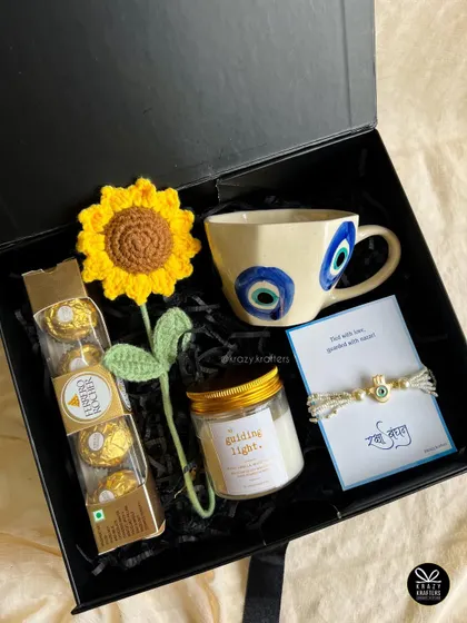 The 'Jigar Ka Tukda' hamper for your sister, themed around the protective evil eye. It features an evil eye mug, a matching rakhi, a crochet sunflower, and her favorite chocolates.