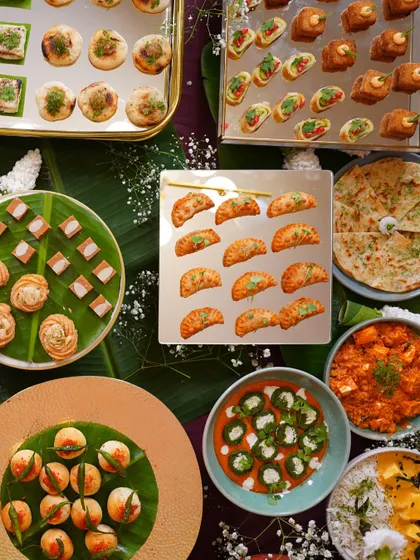 An overhead view of a diverse festive spread, showcasing a variety of Indian appetizers. You can see mini samosas, paneer bites, dhokla, and other savory treats, beautifully arranged on banana leaves and colorful plates.