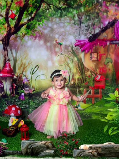 A sweet toddler dressed as a fairy in a pink and green tutu, standing in a whimsical enchanted garden. The colorful backdrop and her happy expression make for a magical portrait.
