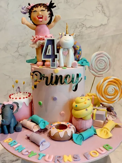 A whimsical cake for a 4th birthday, featuring a cute girl figurine, a unicorn, an elephant, and lots of candy-themed decorations like lollipops and donuts.