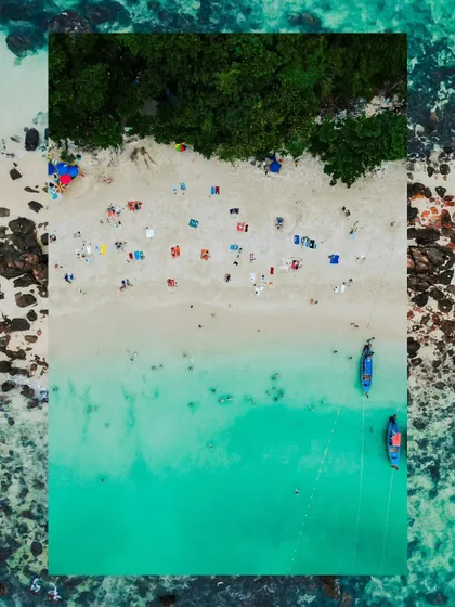 A creative, top-down drone shot of a beach in Thailand, framed to create an artistic composition. This view highlights the patterns of people, umbrellas, and boats against the sand and sea.