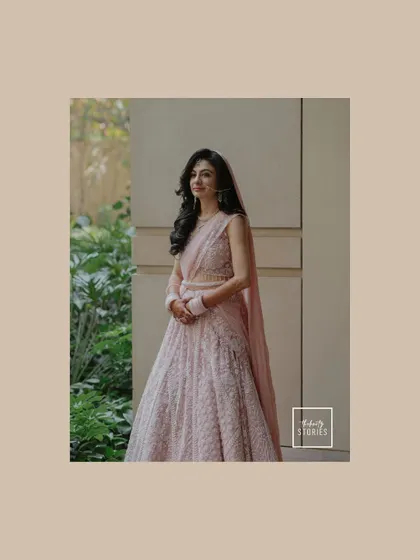A three-quarter portrait of the bride in her beautiful pink lehenga, captured in soft, natural light against a green backdrop.